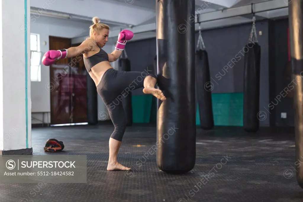 Strong caucasian woman exercising at gym, boxing using punching bag. strength and fitness cross training for boxing.