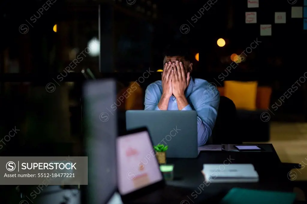 Mixed race businessman working at night, sitting at desk and using laptop. working late in business at a modern office.