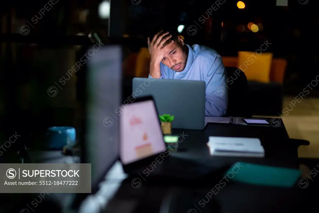 Mixed race businessman working at night, sitting at desk and using laptop. working late in business at a modern office.