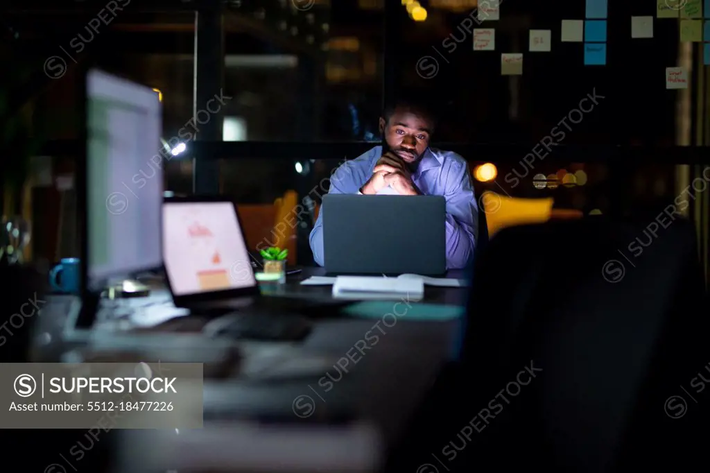 African american businessman working at night, sitting at desk and using laptop. working late in business at a modern office.