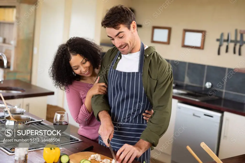 Happy diverse couple in kitchen preparing food together chopping vegetables. spending time off at home in modern apartment.