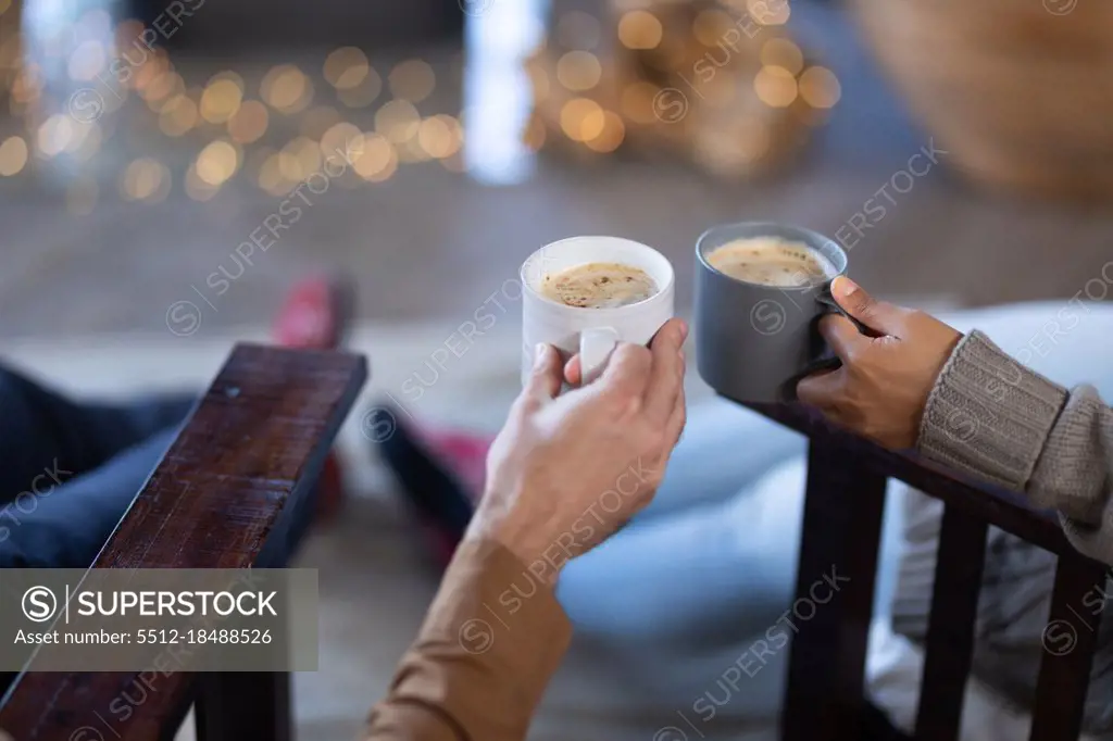 Happy diverse couple in living room holding mugs and drinking coffee. spending time off at home.