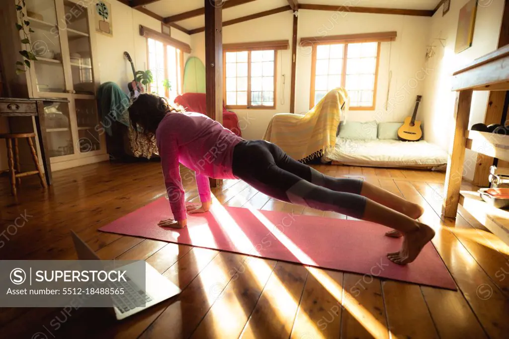 Mixed race woman practicing yoga, doing push ups in sunny living room. healthy lifestyle, enjoying leisure time at home.