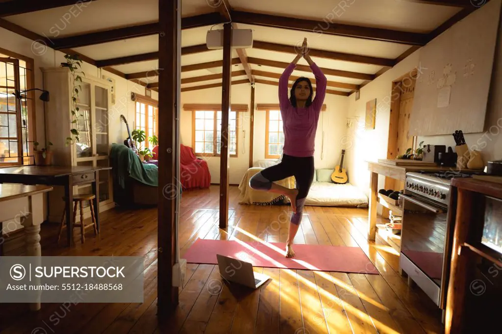 Mixed race woman practicing yoga in sunny living room. healthy lifestyle, enjoying leisure time at home.