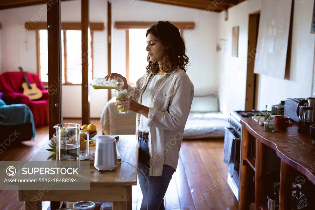 Mixed race woman preparing healthy drink in kitchen. healthy lifestyle, enjoying leisure time at home.