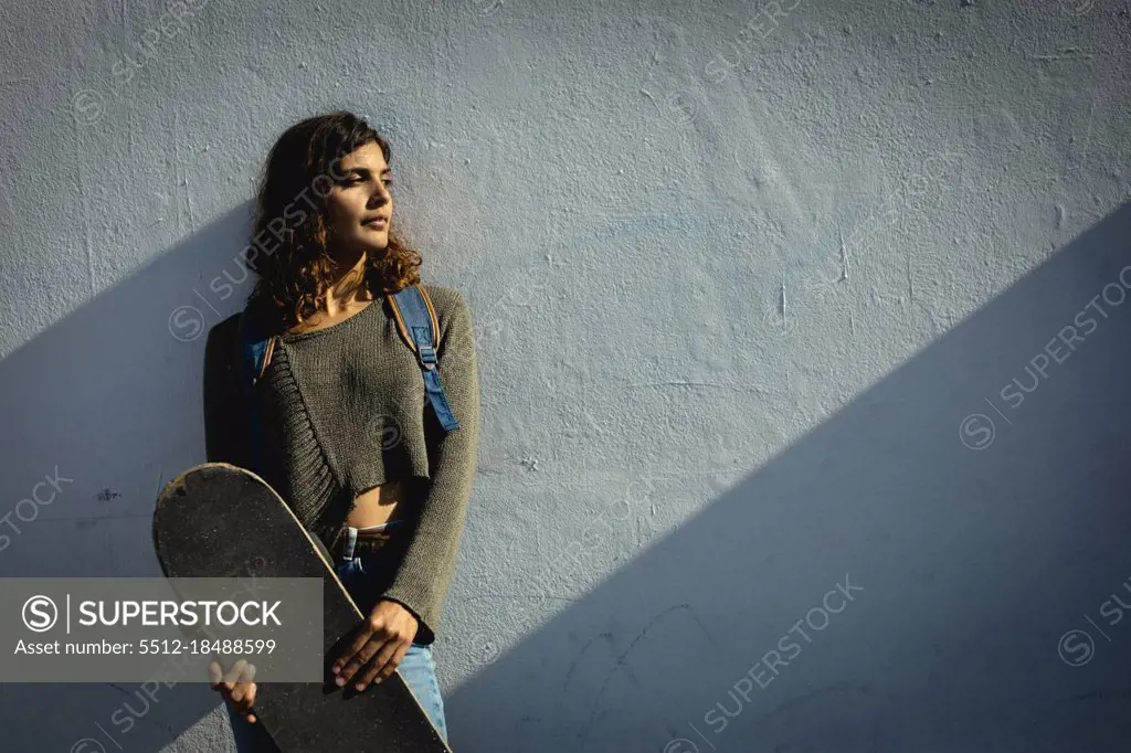 Mixed race woman holding skateboard on sunny day in the street. healthy lifestyle, enjoying leisure time outdoors.