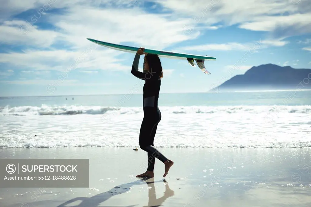 Mixed race woman holding surfboard on sunny day at beach. healthy lifestyle, enjoying leisure time outdoors.