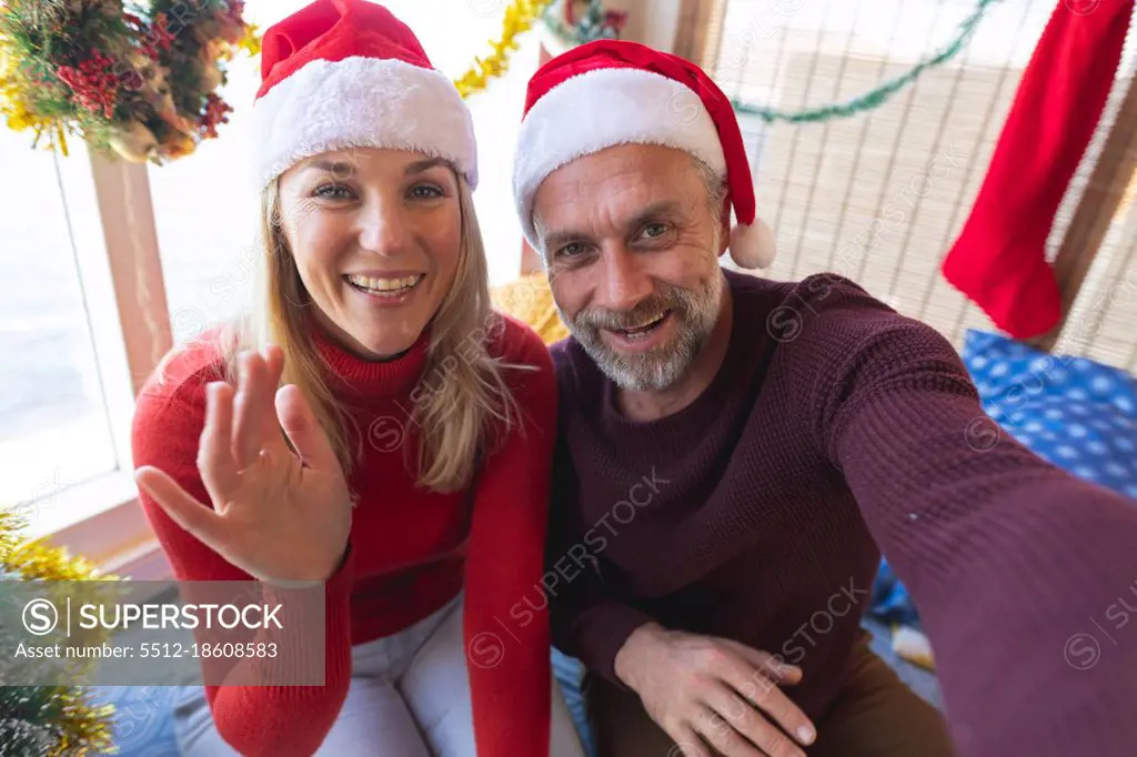 Happy caucasian mature couple wearing santa hats making a video call at christmas. christmas, festivity and communication technology.