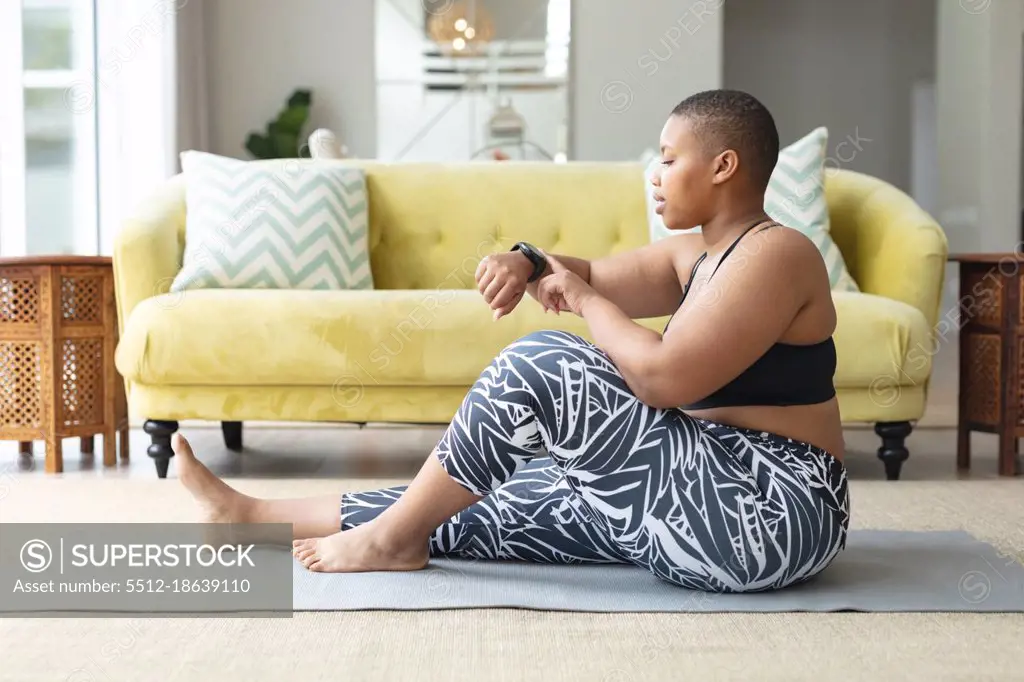 African american plus size woman practicing yoga on mat, checking smartwatch. fitness and healthy, active lifestyle.