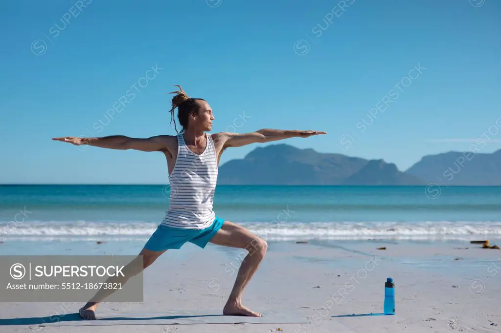 Man practicing warrior 2 pose yoga with arms outstretched at beach against sky with copy space. fitness and healthy lifestyle.