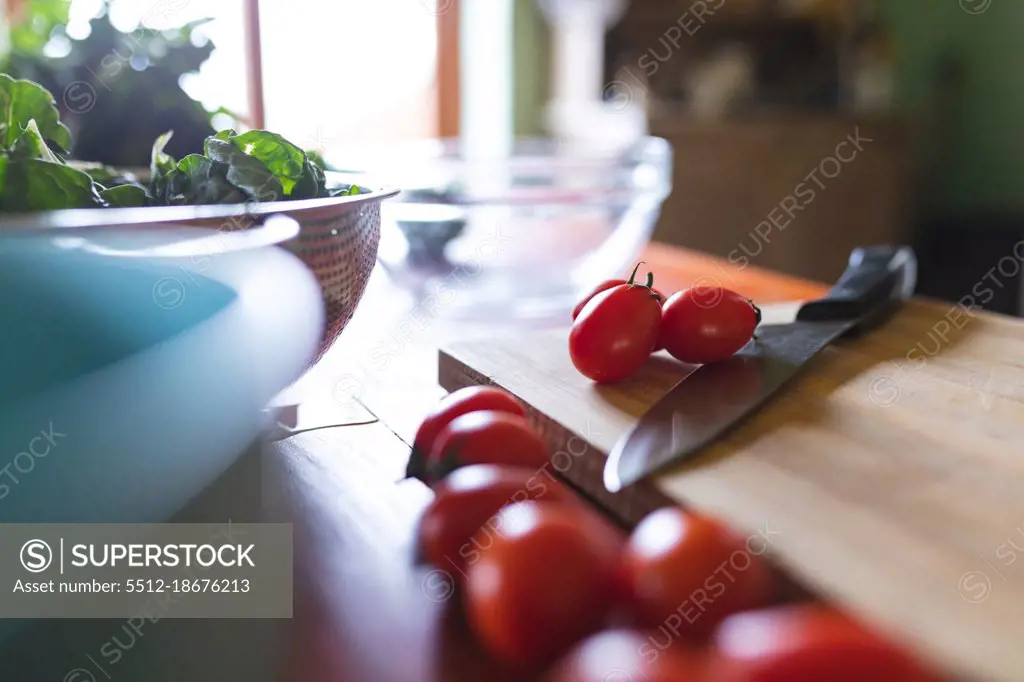 Close-up of fresh red cherry tomatoes with knife on wooden cutting board in kitchen. organic and healthy eating.