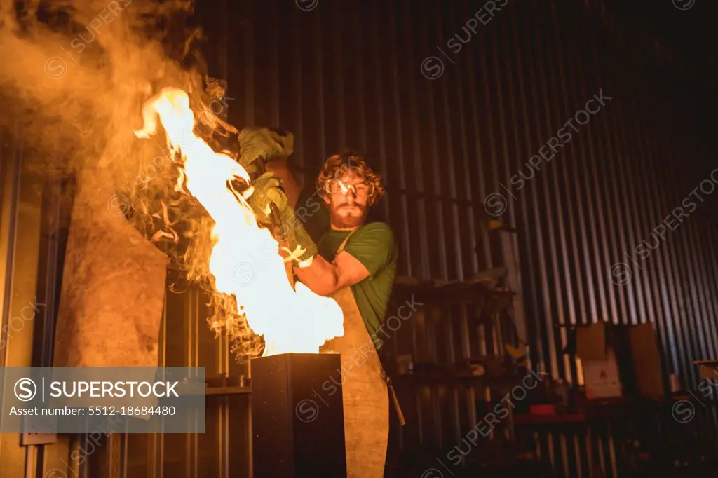 Blacksmith putting metal in fire while forging in manufacturing industry. forging, metalwork and manufacturing industry.