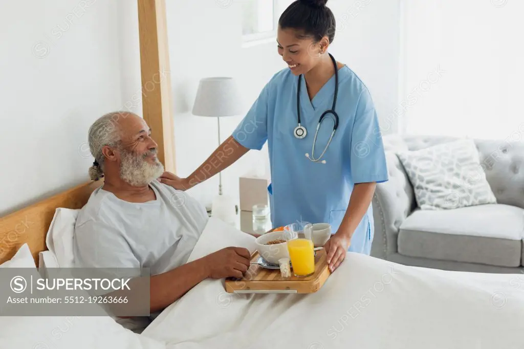 Side view of mixed race healthcare worker talking with old man in bed. Authentic Senior Retired Life Concept