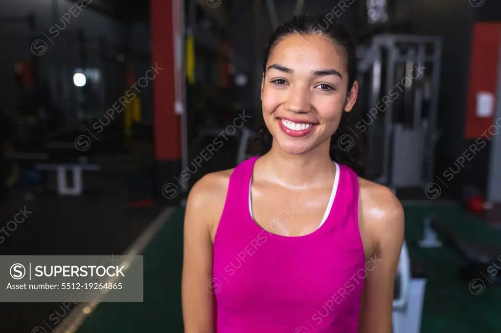 Close-up of Caucasian female athletic looking at camera while standing in fitness center. Bright modern gym with fit healthy people working out and training