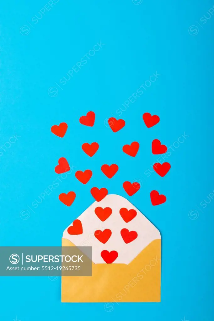 Overhead view of red hearts coming out from yellow envelope over blue background, copy space. valentine's day and love concept.