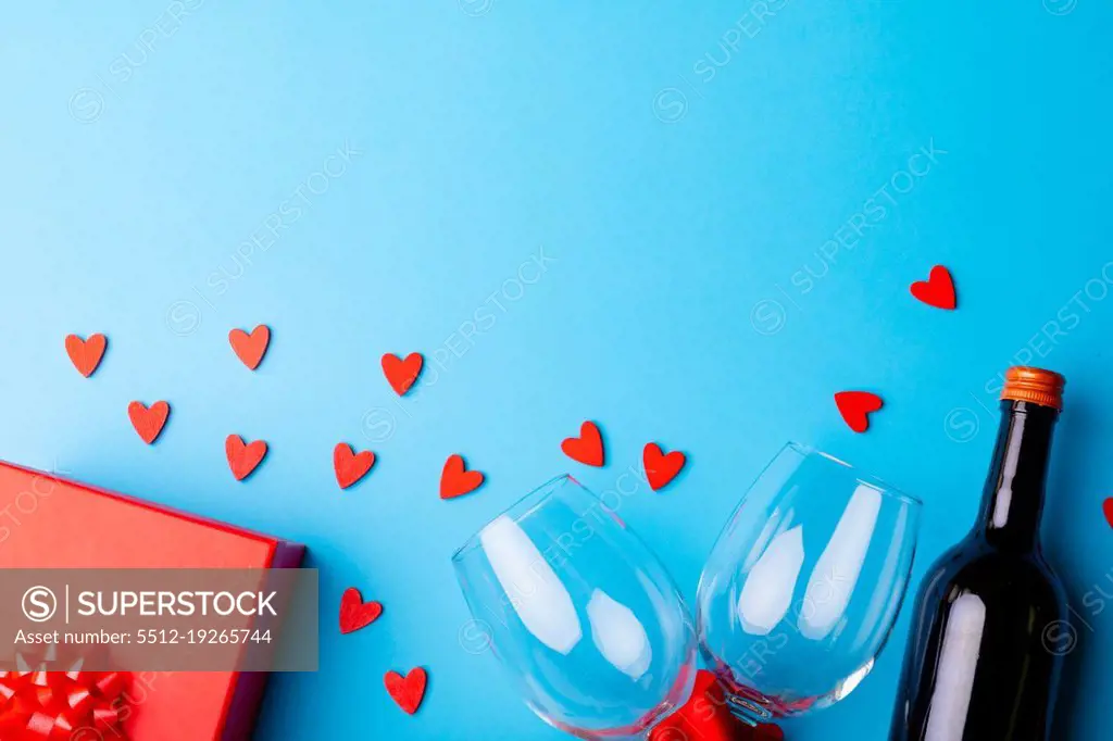 Heart shaped decoration with wineglasses and bottle by gift on blue background, copy space. valentine's day, drink and love concept.