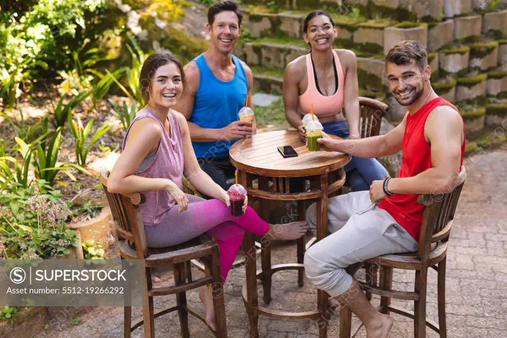 Portrait of happy men and women in sportswear sitting with healthy drinks at table in park. healthy lifestyle, drink and fitness.