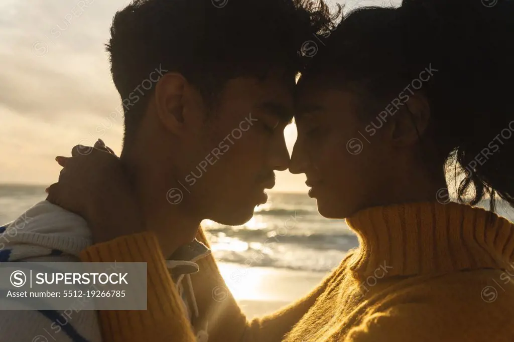 Side view of multiracial couple romancing while hugging each other at beach during sunset. lifestyle, love and weekend.