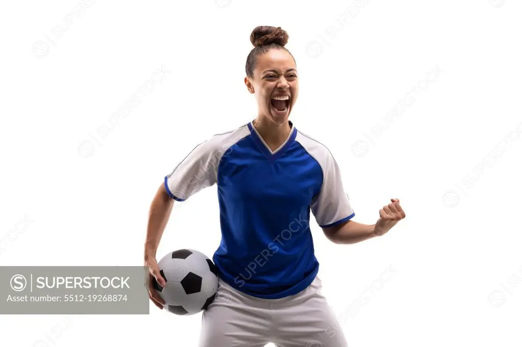 Biracial young female player shouting while standing with clenched fist and soccer ball. white background, unaltered, sport, sports uniform, copy space, victory, athlete and women's soccer.