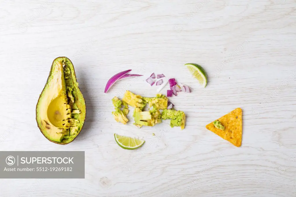 Directly above shot of halved avocado and ingredients on table. unaltered, unhealthy food, snack, preparation, nacho chip, crunchy and savory food.