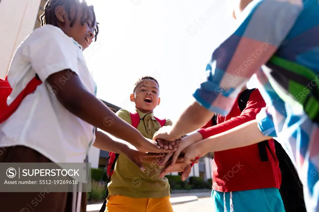 Multiracial schoolboys stacking hands while standing in school campus. unaltered, childhood, education, together, sunny and back to school concept.