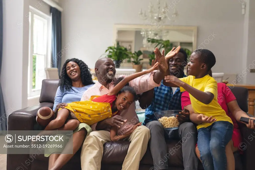 Happy african american multi-generational family high-fiving while watching rugby match on tv. unaltered, lifestyle, sport, fans, family, watching tv, rugby match, cheering and leisure concept.