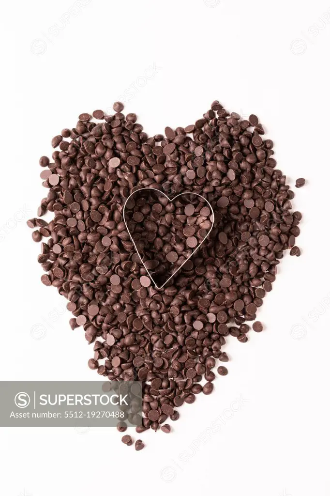 Overhead view of heart shape pastry cutter over chocolate chips on white background. unaltered, sweet food and unhealthy eating concept.