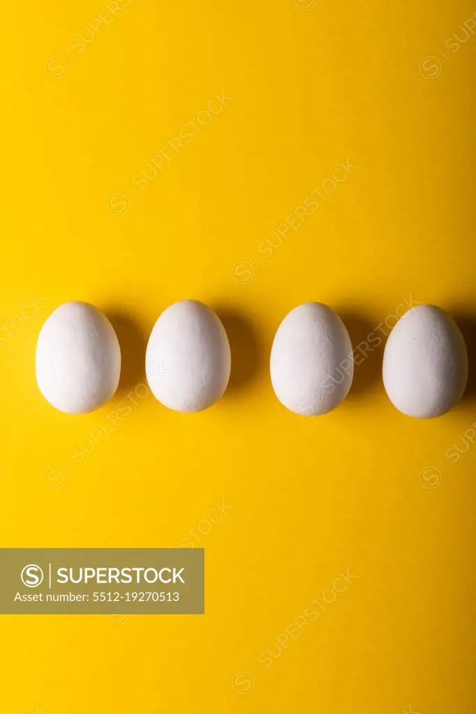 Directly above view of fresh white eggs arranged side by side against yellow background. unaltered, food, healthy eating concept.