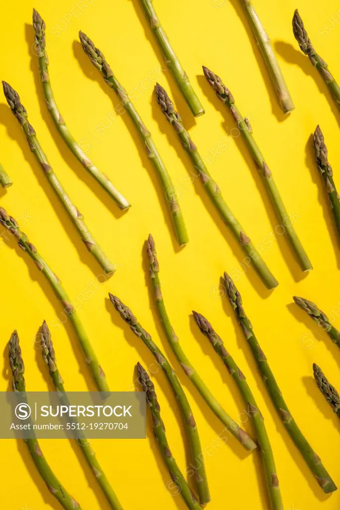 Overhead view of scattered raw green asparagus over yellow background. unaltered, food, healthy eating and organic concept.