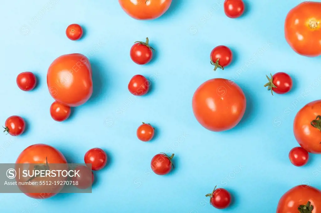 Overhead view of fresh tomatoes scattered over blue background. unaltered, organic food and healthy eating concept.