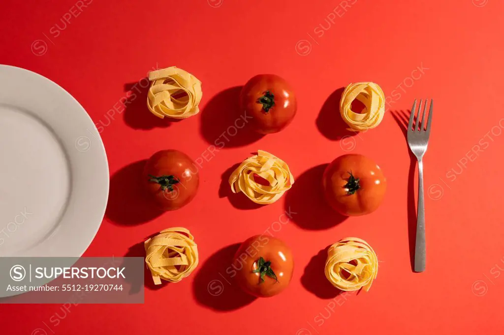 Directly above view of ribbon pasta with tomatoes amidst plate and fork on red background. unaltered, organic food and healthy eating concept.