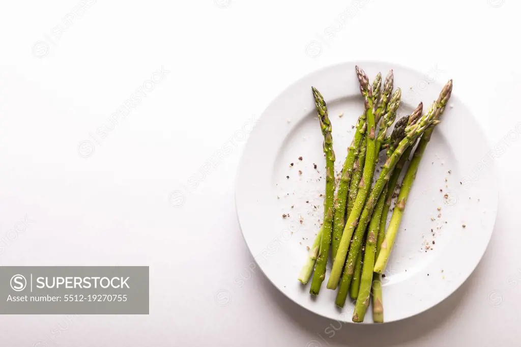 Overhead view of asparagus and seasoning in plate by copy space against white background. unaltered, food, healthy eating and organic concept.