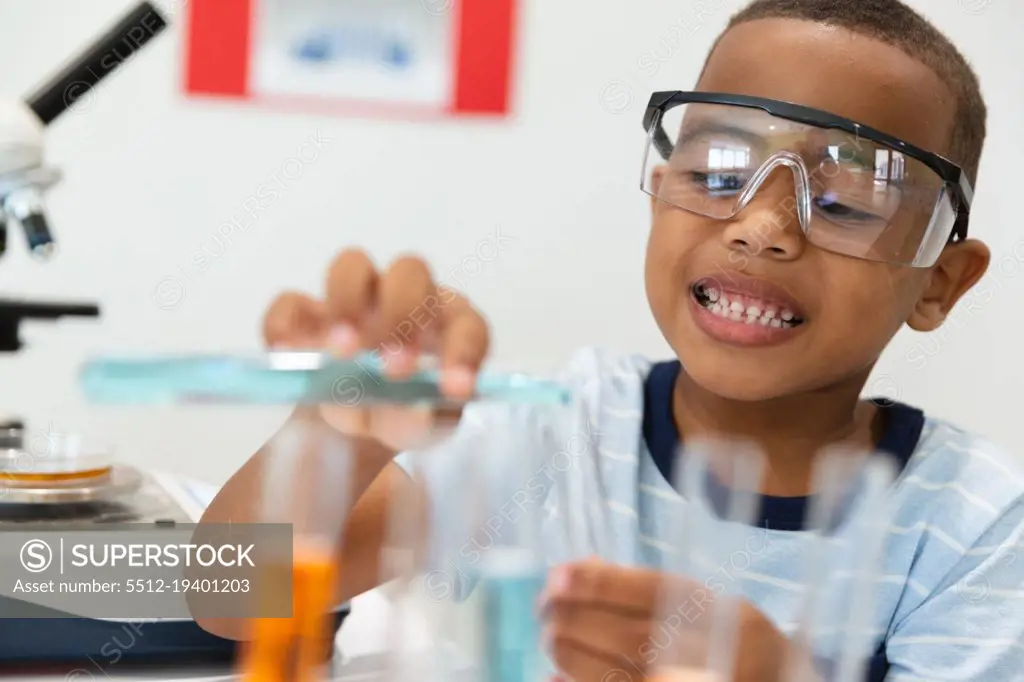 Smiling african american elementary schoolboy performing chemistry practical in laboratory. unaltered, education, laboratory, stem, scientific experiment, protection and school concept.