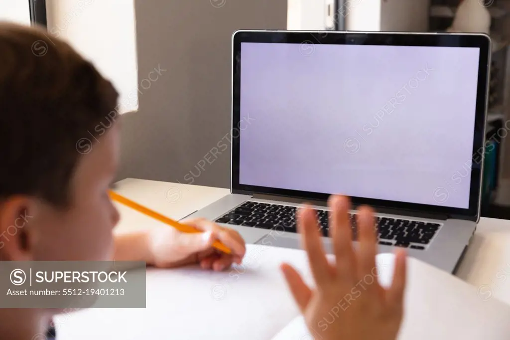 Caucasian elementary schoolboy waving hand on laptop while studying over video conference. unaltered, copy space, education, connection, childhood, studying, wireless technology and school concept.