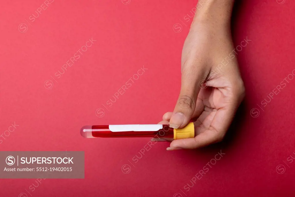 Cropped hand of african american mid adult woman holding test tube with blood on red background. copy space, blood, test tube, medical, sample, laboratory and healthcare concept.