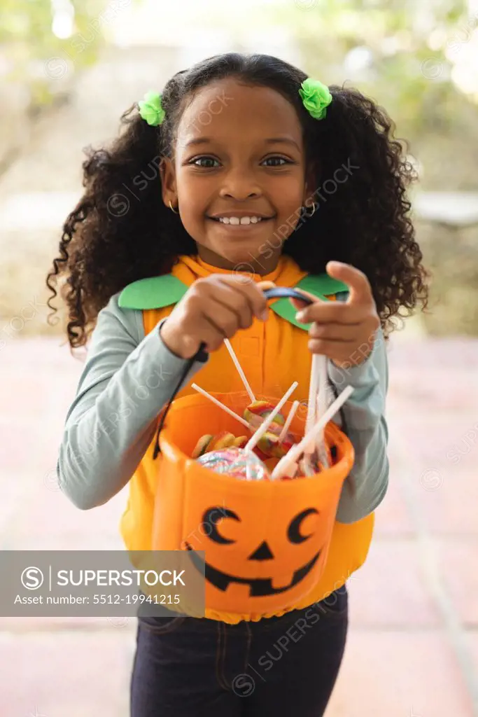 Vertical image of happy african american girl in halloween costume with basket. Halloween, american culture and celebration concept.