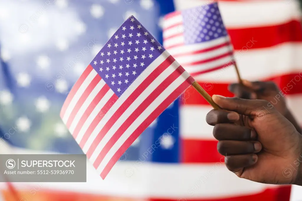 African American hand holding an American flag with another flag in the background. The focus on the flag symbolizes patriotism and national pride.