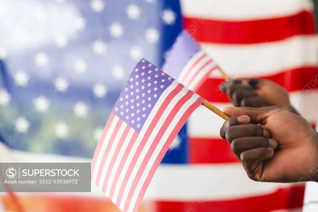 African American hand holding a small American flag, with a larger flag in the background. The focus on the flag suggests a theme of patriotism or national celebration.