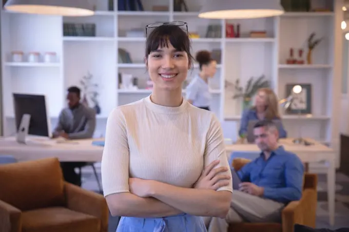 Portrait of a happy Asian businesswoman working in a modern office, looking at camera and smiling, with her colleagues working in the background