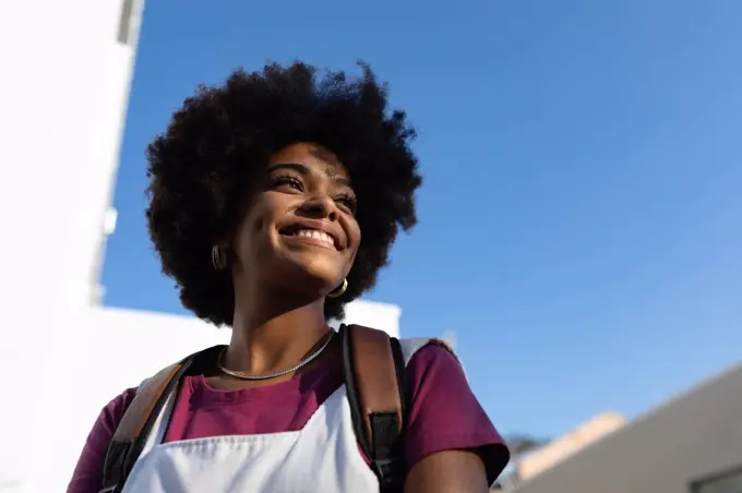 Low angle close up of a young mixed race woman standing and looking away smiling against blue sky