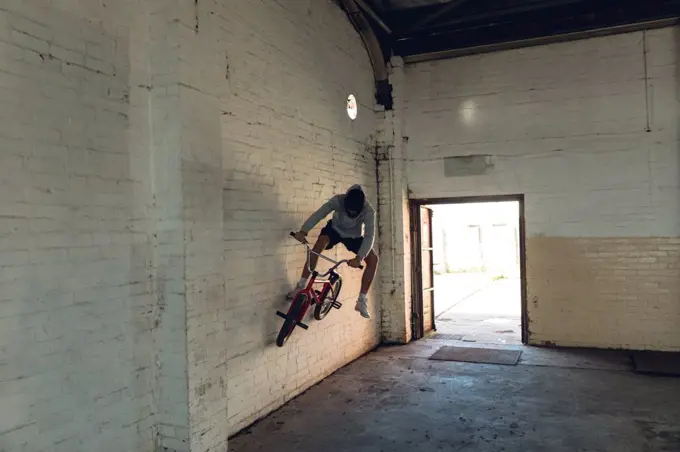 Front view of a young Caucasian man wallriding a BMX bike in an empty corridor at an abandoned warehouse