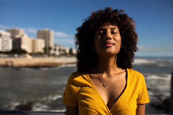 Front view of a young mixed race woman with eyes closed on a sunny day by the sea