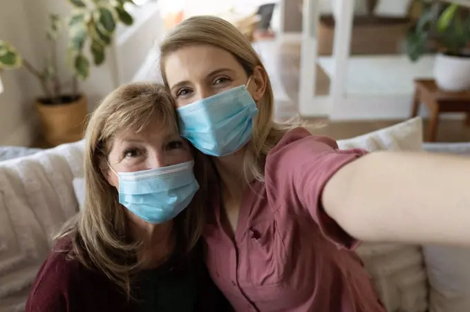 Senior Caucasian woman spending time at home with adult daughter,sitting on couch talking and using smartphone, taking selfie. Social distancingduring Covid 19 Coronavirus quarantine