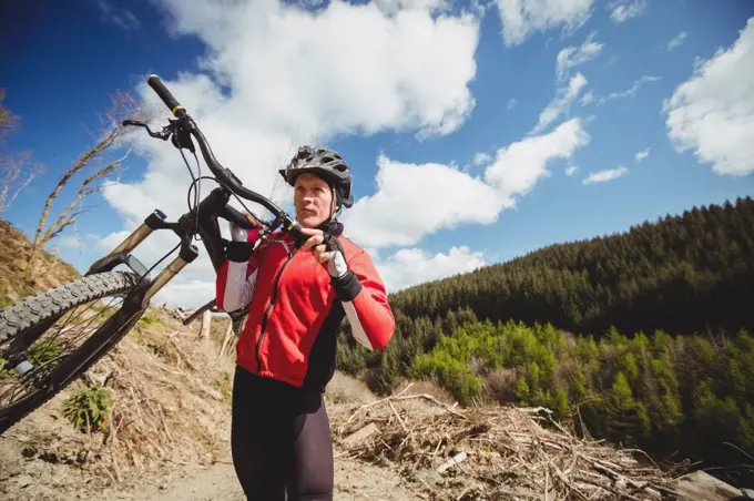 Biker carrying bicycle on mountain against sky