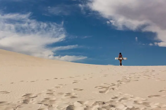 Rear view of woman with sandboard standing in the desert on a sunny day