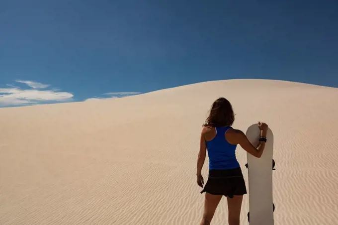 Woman with sandboard standing in the desert on a sunny day