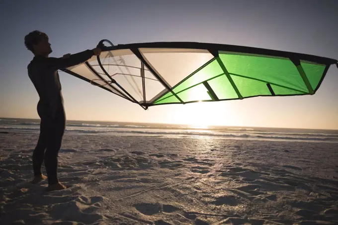 Male surfer holding a kite on the beach at dusk