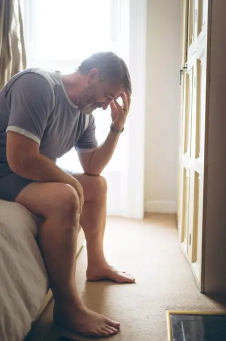 Tensed senior man sitting on bed in bedroom at home