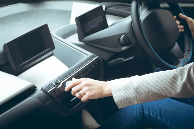 Mid section of businesswoman using music system while driving car