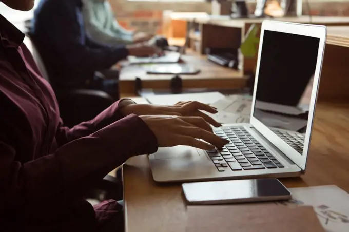 Mid section of executive using laptop at desk in office